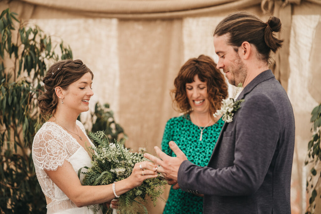 Elliot Photo Bride and groom exchanging rings during an intimate ceremony with celebrant, Amy Lee, smiling nearby